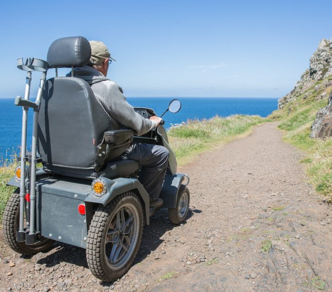 senior man riding a mobility scooter or tramper over rough terrain in an independence concept image